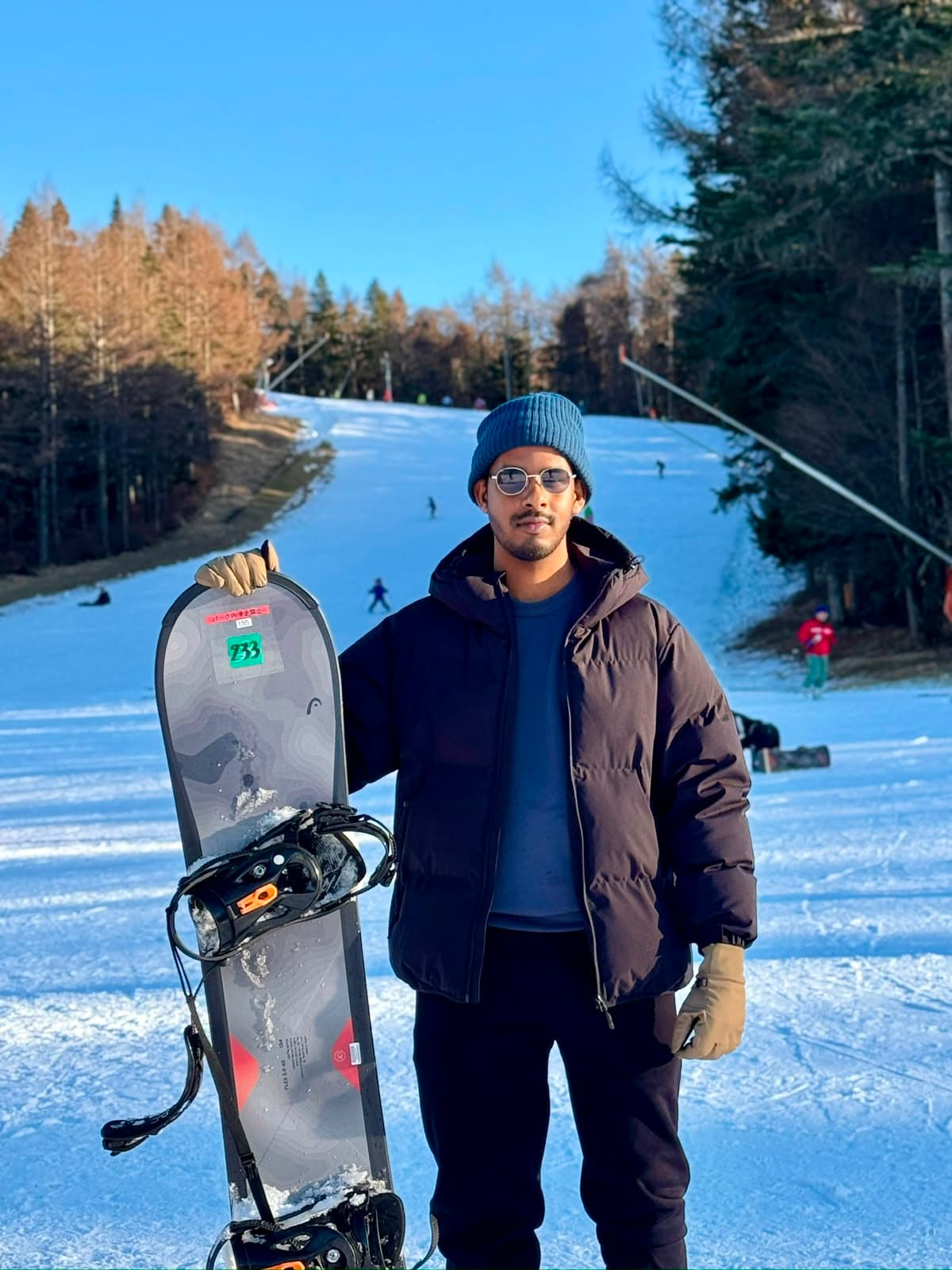 Vihanga Nimesha standing on a ski slope holding a snowboard